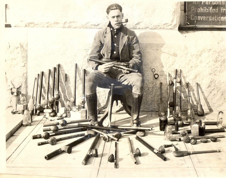 A police officer poses with opium pipes, opium lamps, and other paraphernalia confiscated at opium den raids in San Francisco. 