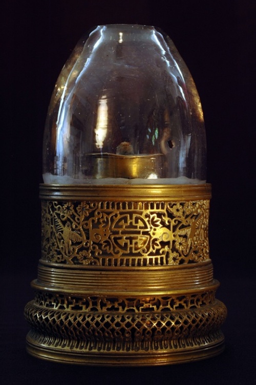 A brass opium lamp with openwork in floral and bird motifs. The threaded base indicates this lamp once had a lid to protect the glass chimney when it was not in use.