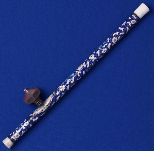 A rare opium pipe adorned with Canton enamel. Within the enamel-covered copper sheath is a peeled stem of bamboo. The endpieces are white jade, and the hexagonal pipe-bowl is ceramic.