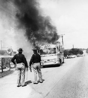 State troopers watch as a Freedom Rider bus burns after being firebombed on May 14, 1961. Via the Birmingham Civil Rights Institute.
